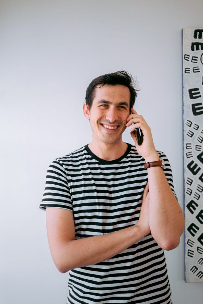Young man smiling while talking on mobile phone, wearing striped shirt, indoors.